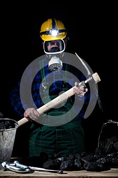 A miner with a protective helmet on and a flashlight and dust mask in his hands holds a mining cliff