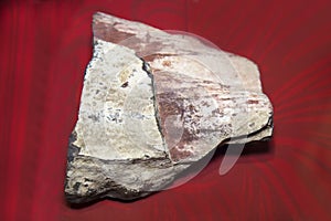 The mineral is Ferruginous quartzite crumpled into small folds on a red background. Mineralogy