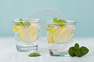 Mineral infused water with limes, lemons, ice and mint leaves on blue background, homemade detox soda water