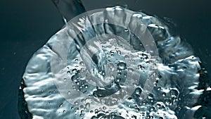 Mineral water pouring transparent glass closeup. Blebs going up smooth liquid