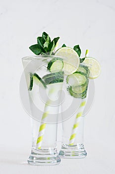 Mineral water with slices cucumber, ice, lime, mint on white wood table with copy space.