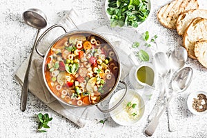 Minestrone soup in a pan on a light table, top view. Italian soup with pasta and seasonal vegetables. Delicious vegetarian food co