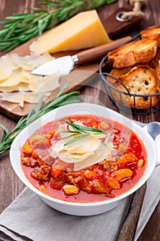Minestrone soup served with crispy bread, on wooden background, vertical