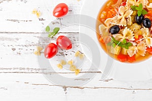 Minestrone, vegetarian soup with pasta and vegetables on white wooden rustic background. Traditional italian food