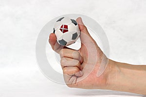 Mini ball of football in hand and one black point is Denmark flag, hold it with two finger on white background.