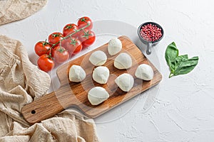 Mini balls of mozzarella cheese, on chop wood board ingredients for salad Caprese. over white background. Top view