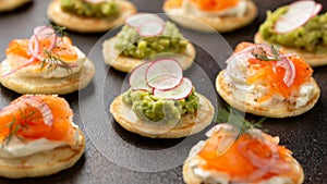 Mini blini pancakes with soft cheese, cold smoked salmon and guacamole