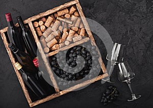 Mini bottles of red wine and empty glasses with dark grapes with corks and opener inside vintage wooden box on black stone