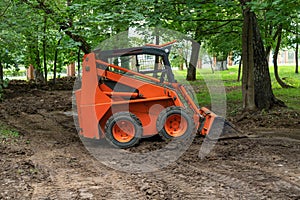 Mini bulldozer or skid steer loader working with earth in public park and performing landscaping works