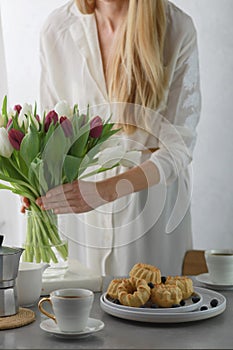 Mini bundt cakes with fruits on plate, cup of coffee and girl put bouquet of tulip flowers in a vase.