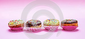 Mini cakes with icing and colorful sprinkles on pink background