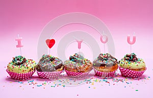 Mini cakes with icing and colorful sprinkles on pink background, text I love you