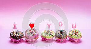 Mini cakes with icing and colorful sprinkles on pink background, text I love you