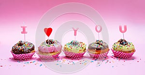 Mini cakes with icing and colorful sprinkles on pink background, text I love you