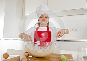 Mini chef girl with cook hat and apron mixing flour and eggs baking preparing sweet desert smiling happy