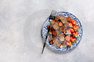 Mini chocolate pancake cereal with strawberries for breakfast on gray concrete table. Trendy home breakfast with tiny pancakes.