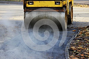 Mini compactor tires the upper layer of asphalt in the construction of a bicycle lane. Steaming hot asphalt, reportage shooting.