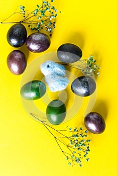 Mini composition of Easter holiday. painted colored eggs, bunny toy and twigs of spring flowers. top view. yellow