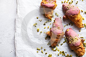 Mini-croissants with ruby chocolate and pistachios on a baking paper, gray background. Top view and copy space