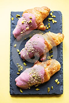 Mini-croissants with ruby chocolate and pistachios on a slate board. Overhed view