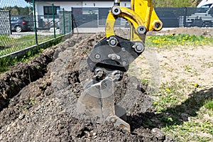 Mini digger digging a hole in the garden along the fence to the drainage pipes.