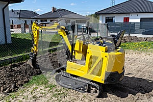 Mini digger digging a hole in the garden along the fence to the drainage pipes.