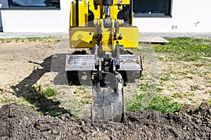 Mini digger digging a hole in the garden along the fence to the drainage pipes.