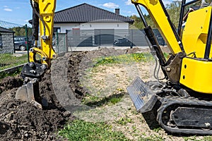 Mini digger digging a hole in the garden along the fence to the drainage pipes.