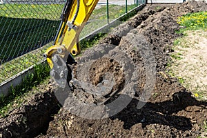 Mini digger digging a hole in the garden along the fence to the drainage pipes.