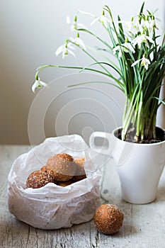 Mini donuts in a paper bag and snowdrops flowers on a white, woode table