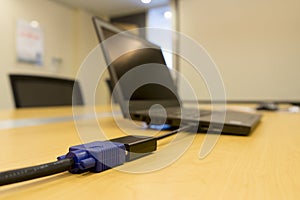 A mini-DVI from laptop to VGA video cable projector on wooden table in meeting room