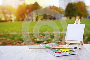 Mini easel, paint and brush on the background of the city park. Draw a landscape in city park. Artist and painting concept.