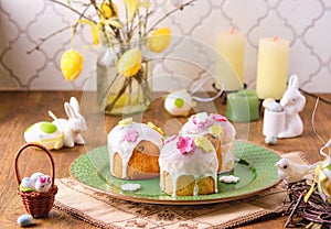 Mini Easter cakes covered with icing and decorated with sugar flowers on a green plate on a wooden background. Easter table,