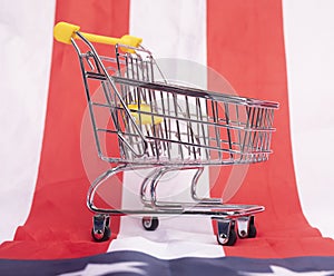 Mini empty supermarket shopping cart over American flag. Consuption concept