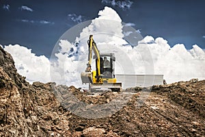 Mini excavator at the construction site on the edge of a pit against a cloudy blue sky. Compact construction equipment for