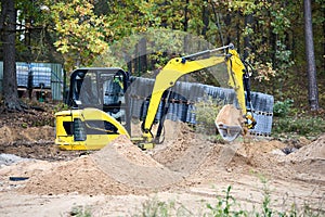 Mini excavator at construction site surrounded by trees. Compact construction equipment for operative earthworks. Tracked yellow