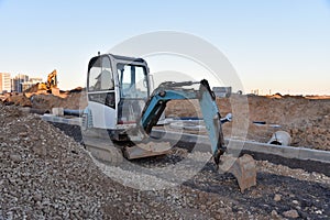 Mini excavator digg trench to lay cables concrete curbs and paving slabs at construction site. Backhoe on earthwork/roadworks