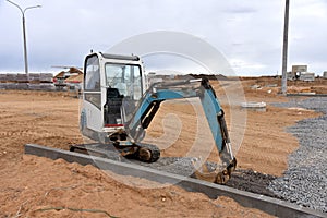 Mini excavator digg trench to lay cables concrete curbs and paving slabs at construction site. Backhoe on earthwork/roadworks