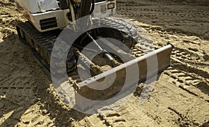 Mini excavator parked on brown dirt with blade and track in closeup