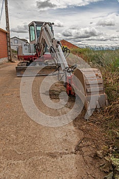 Mini excavator in the process of repairing a street in a rural area