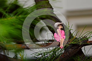 Mini figure of girl with cowboy hat and pink dress sitting on branch of tree