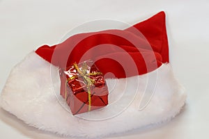 Mini gift box in red reflect gift wrap with golden rope knot and red white christmas hat isolated on white background.