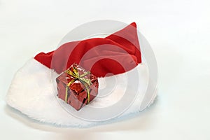 Mini gift box in red reflect gift wrap with golden rope knot and red white christmas hat isolated on white background.