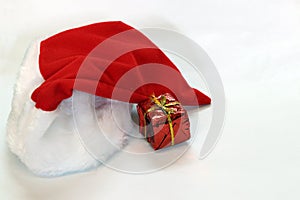 Mini gift box in red reflect gift wrap with golden rope knot and red white christmas hat isolated on white background.