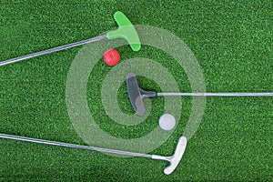 Mini-golf clubs and balls of different colors laid on artificial grass