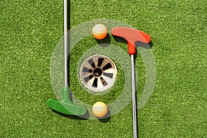 Mini-golf clubs and balls of different colors laid on artificial grass.