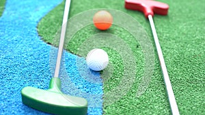 Mini-golf clubs and balls of different colors laid on artificial grass.