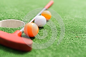 Mini-golf clubs and balls of different colors laid on artificial grass.