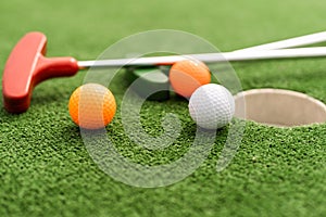 Mini-golf clubs and balls of different colors laid on artificial grass.