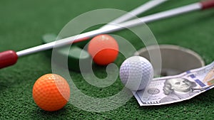 Mini-golf clubs and balls of different colors laid on artificial grass.